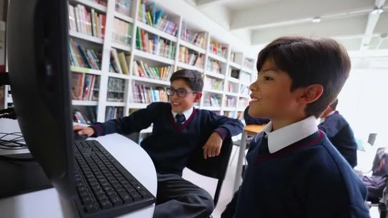 Two students working together at a desktop computer in a library